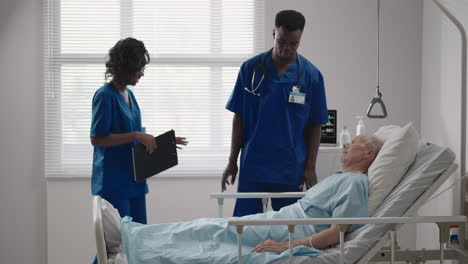 Senior-patient-on-bed-talking-to-2-African-American-doctor-in-hospital-room-Health-care-and-insurance-concept.-Doctor-comforting-elderly-patient-in-hospital-bed-or-counsel-diagnosis-health.